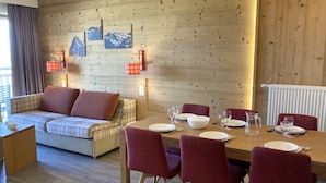 Une pièce chaleureuse avec un mur en bois, un canapé, une table à manger dressée avec des assiettes et des verres, et un radiateur.