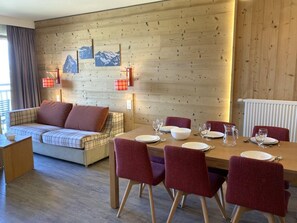 A cozy room with a wooden wall, a sofa, a dining table set with plates and glasses, and a radiator. - 300m from resort center, 4th floor, balcony, tv, ski locker, 62m², Avoriaz (Avoriaz)