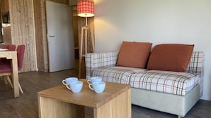 Un salon chaleureux avec un canapé à carreaux, une table basse en bois sur laquelle sont posées des tasses, et une lampe rouge.