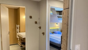Un couloir étroit mène à une chambre où se trouve un lit superposé, une salle de bain avec un porte-serviettes et une porte bien visible.
