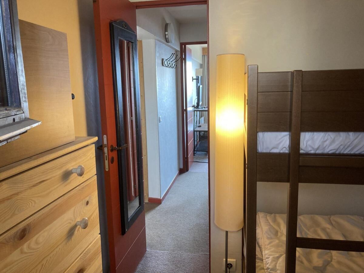 A narrow hallway with a wooden dresser, a door, and a bunk bed with a lamp.