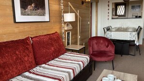 Ein gemütliches Zimmer mit einem gestreiften Sofa, einem roten Sessel, einem Esstisch für vier Personen und einem gerahmten Bild an der Wand.