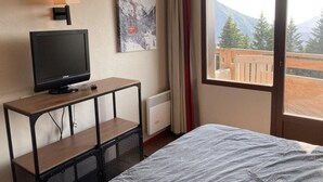 Ein Hotelzimmer mit Bett, Fernseher auf Holzständer, Gemälde an der Wand und Bergblick durch das Fenster.