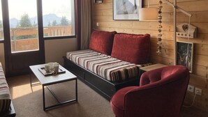Ein gemütliches Zimmer mit einer Couch, einem kleinen Tisch mit Tassen, einem Stuhl und einem Fenster mit Bergblick.
