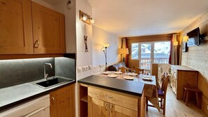 Una cocina compacta con armarios de madera, un lavamanos empotrado y una zona de comedor con una mesa preparada para cuatro comensales.