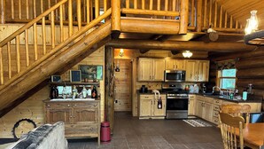 A rustic cabin interior with a wooden staircase, a kitchen with modern appliances, and a dining area. - Up North Retreat near Lake Superior (Port Wing)