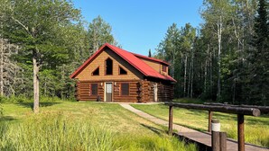 A log cabin with a red roof, a wooden deck, and a pathway leading to the entrance. - Up North Retreat near Lake Superior (Port Wing)