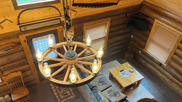 A rustic cabin interior with a wooden ceiling, a central wooden chandelier, a sofa, a small table, and a window with blinds. - Up North Retreat near Lake Superior (Port Wing)