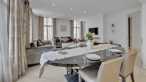 A modern dining area with a round table set for four, a sofa in the background, and a TV mounted on the wall.