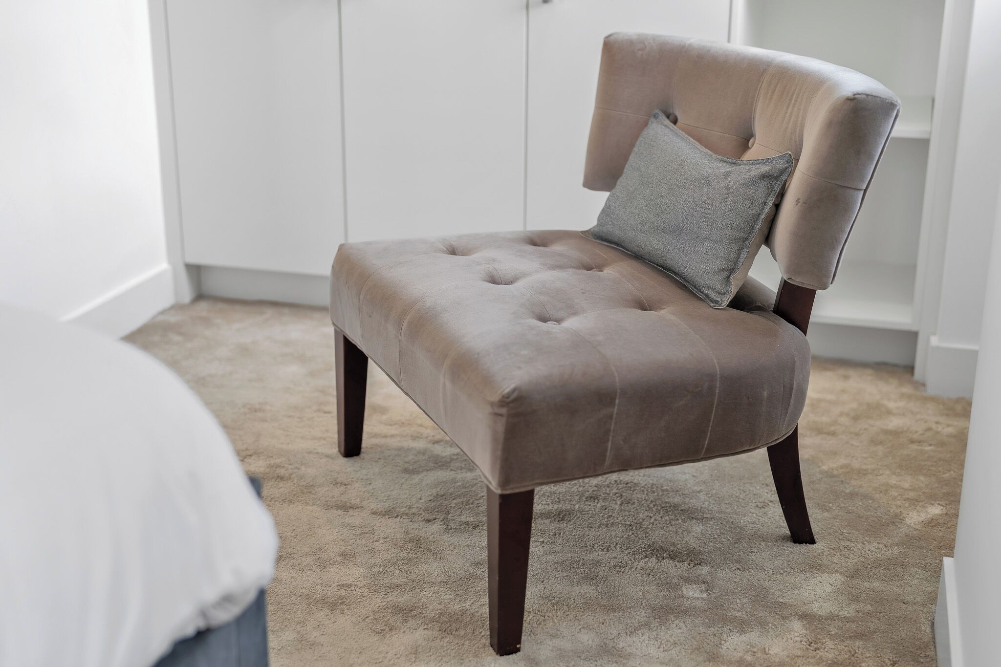 Una poltrona trapuntata con un cuscino, gambe in legno scuro e un pavimento rivestito di moquette.