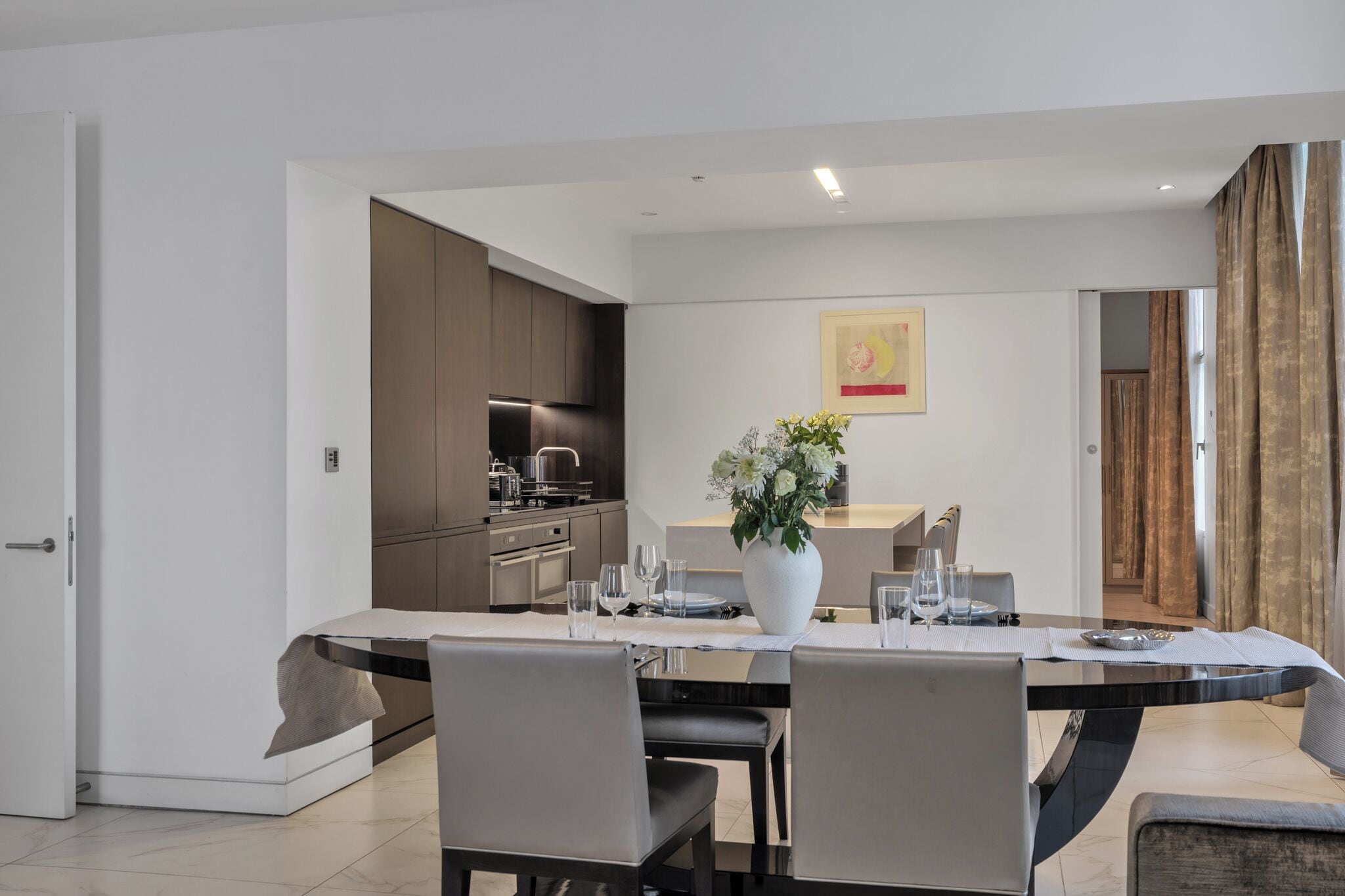 Un espace repas moderne avec une longue table, des chaises et un vase de fleurs.