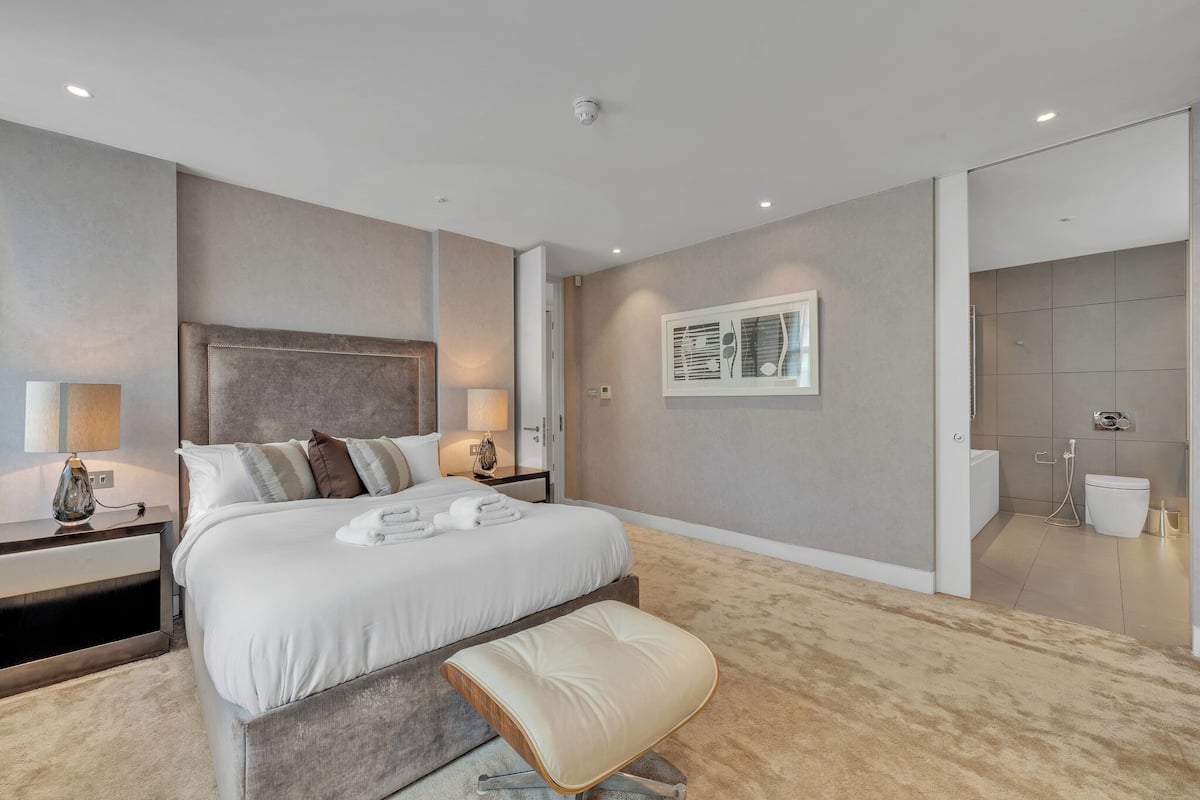 A modern hotel room with a large bed, bedside tables, a bench, a shower, and a toilet.