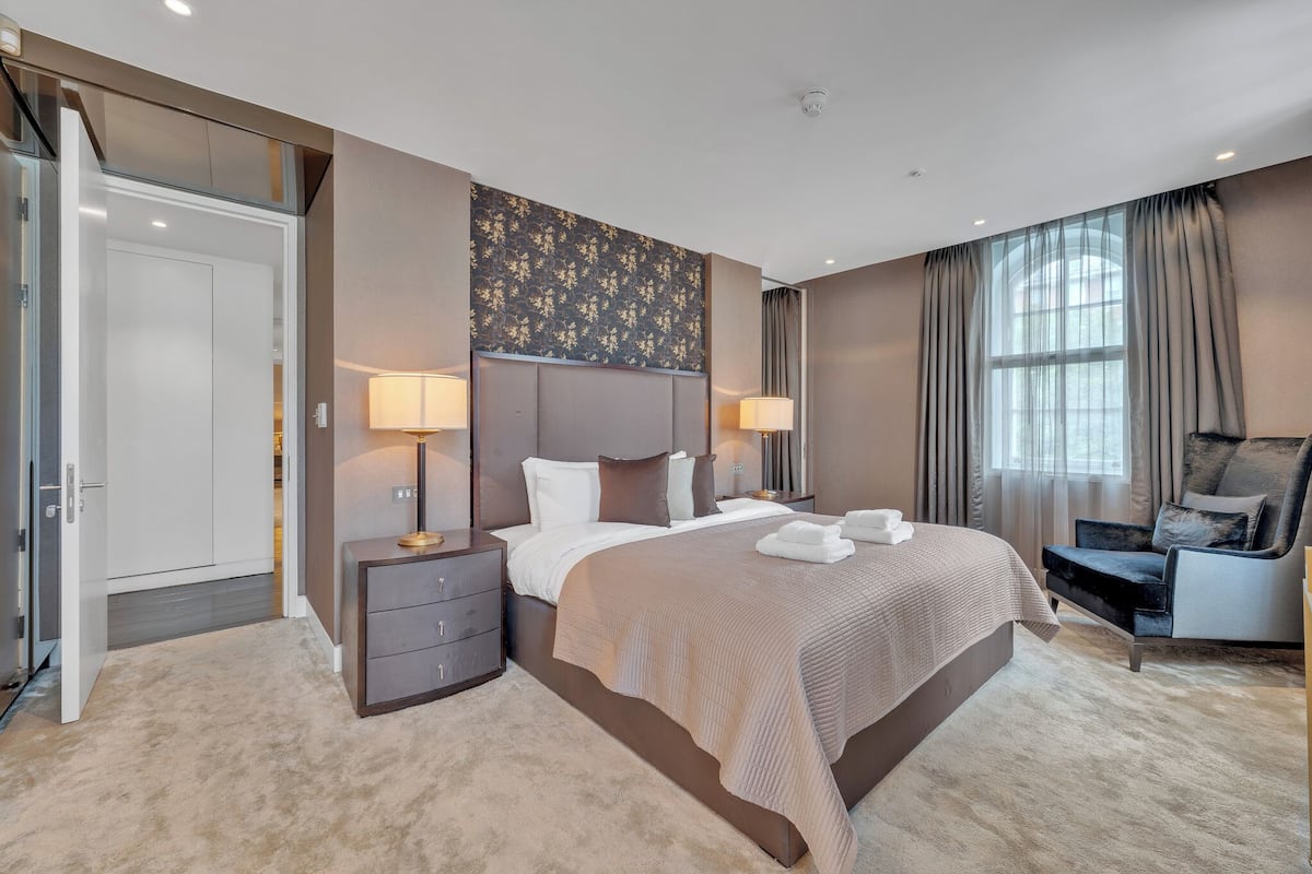 A modern hotel room with a large bed, bedside lamps, a desk, and a chair.