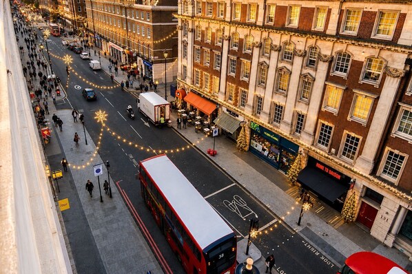 Straßenansicht mit einem roten Doppeldeckerbus, Gebäuden mit Geschäften und einem Hotel namens 'Home to Daisy' mit Weihnachtsdekorationen.