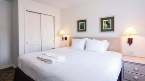 Habitación de hotel con una cama grande, dos lámparas de noche, una mesita de noche y dos cuadros en la pared.