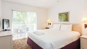 Habitación de hotel con una cama grande, televisión, escritorio y balcón con vistas a árboles.