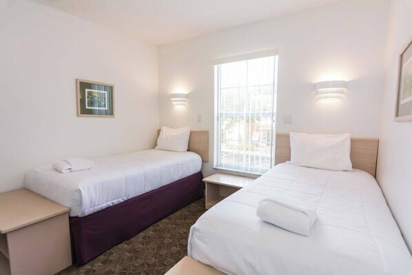 A hotel room with two beds, a window with a view, and wall-mounted lights.