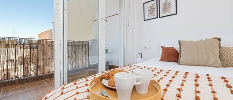 A bedroom with a bed, a bedside table, a tray with cups and a plate, and a view of the outside balcony.
