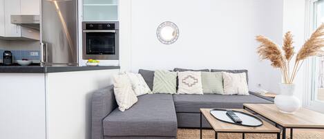 A modern kitchen with a built-in oven and a grey sectional sofa with patterned cushions.