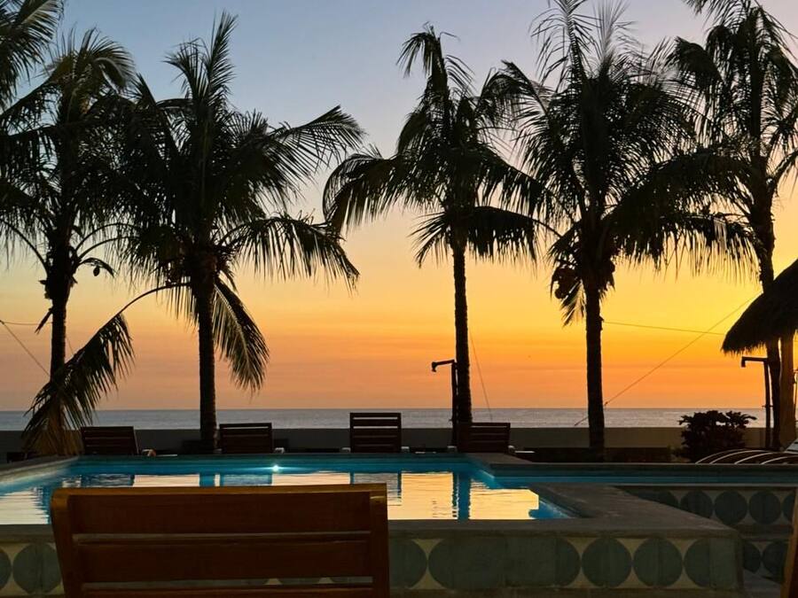 A poolside area with lounge chairs and a view of the sunset over the ocean.