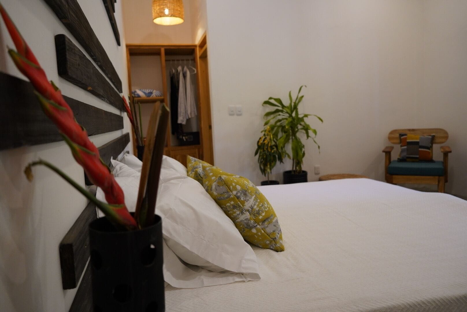A bedroom with a bed, a wooden headboard, a plant, a chair, and a wardrobe.