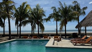 A swimming pool with lounge chairs and palm trees, overlooking a beach. - Hotel Kraken (Tola)