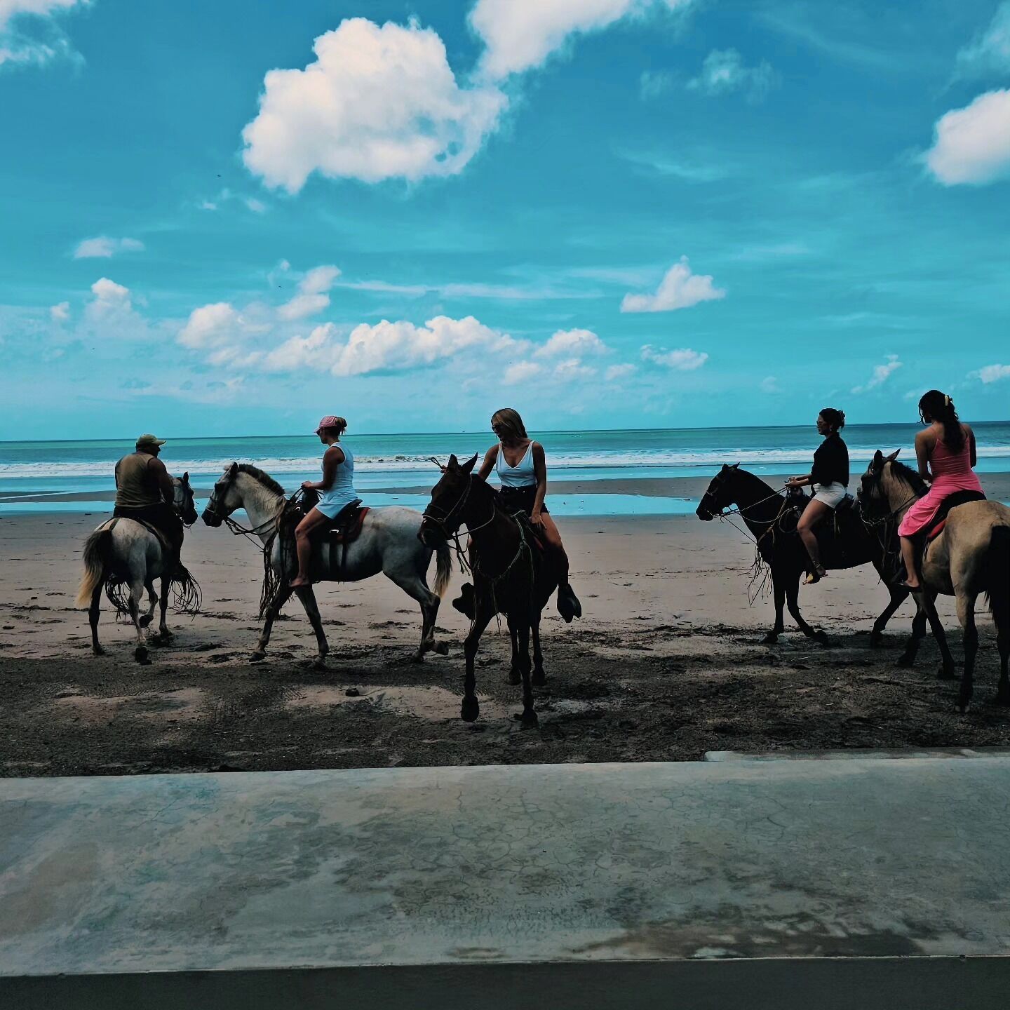 Escena de playa con gente cabalgando a lo largo de la orilla.