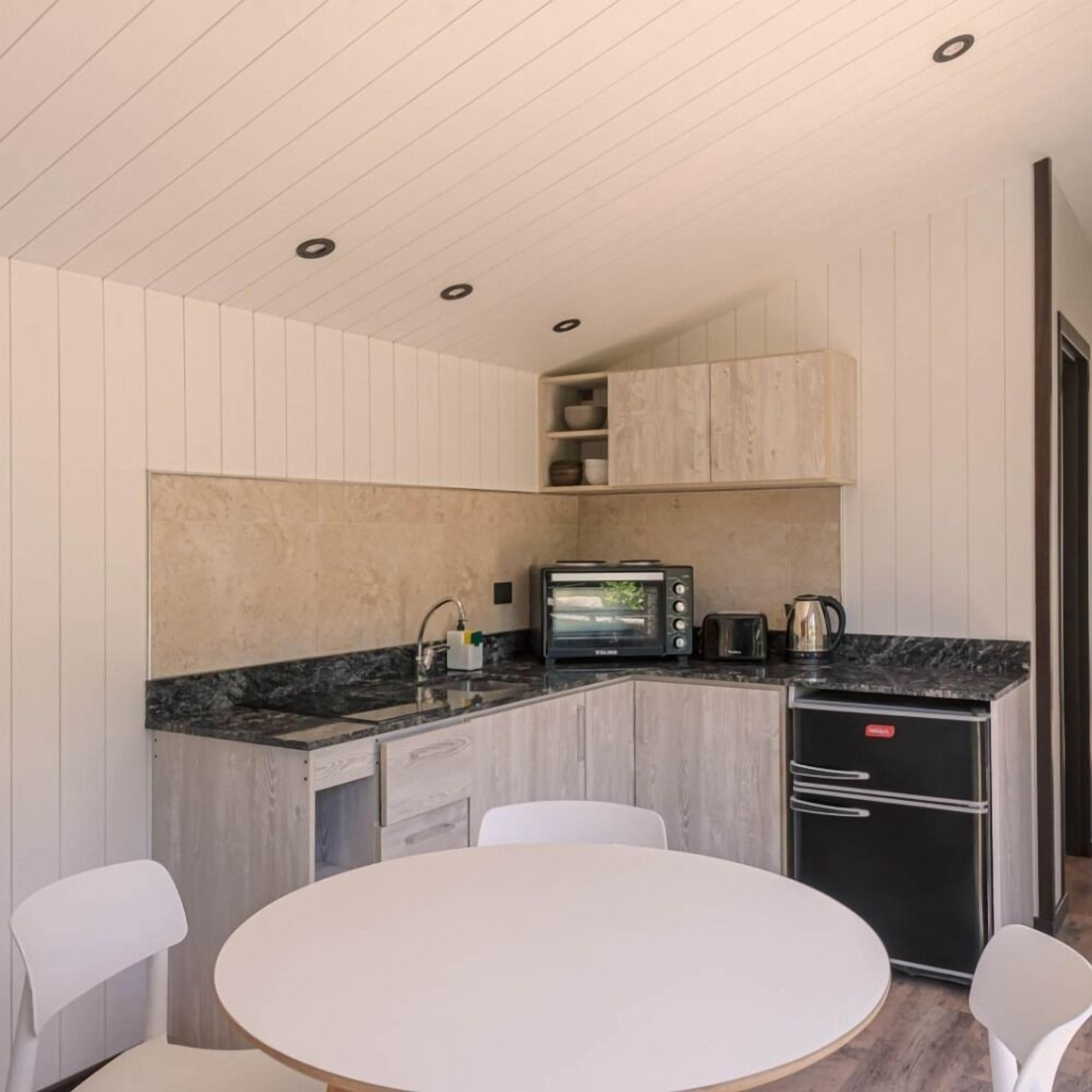 A compact kitchen with a built-in oven, a coffee maker, and a toaster. There is a round table with two chairs in the center.