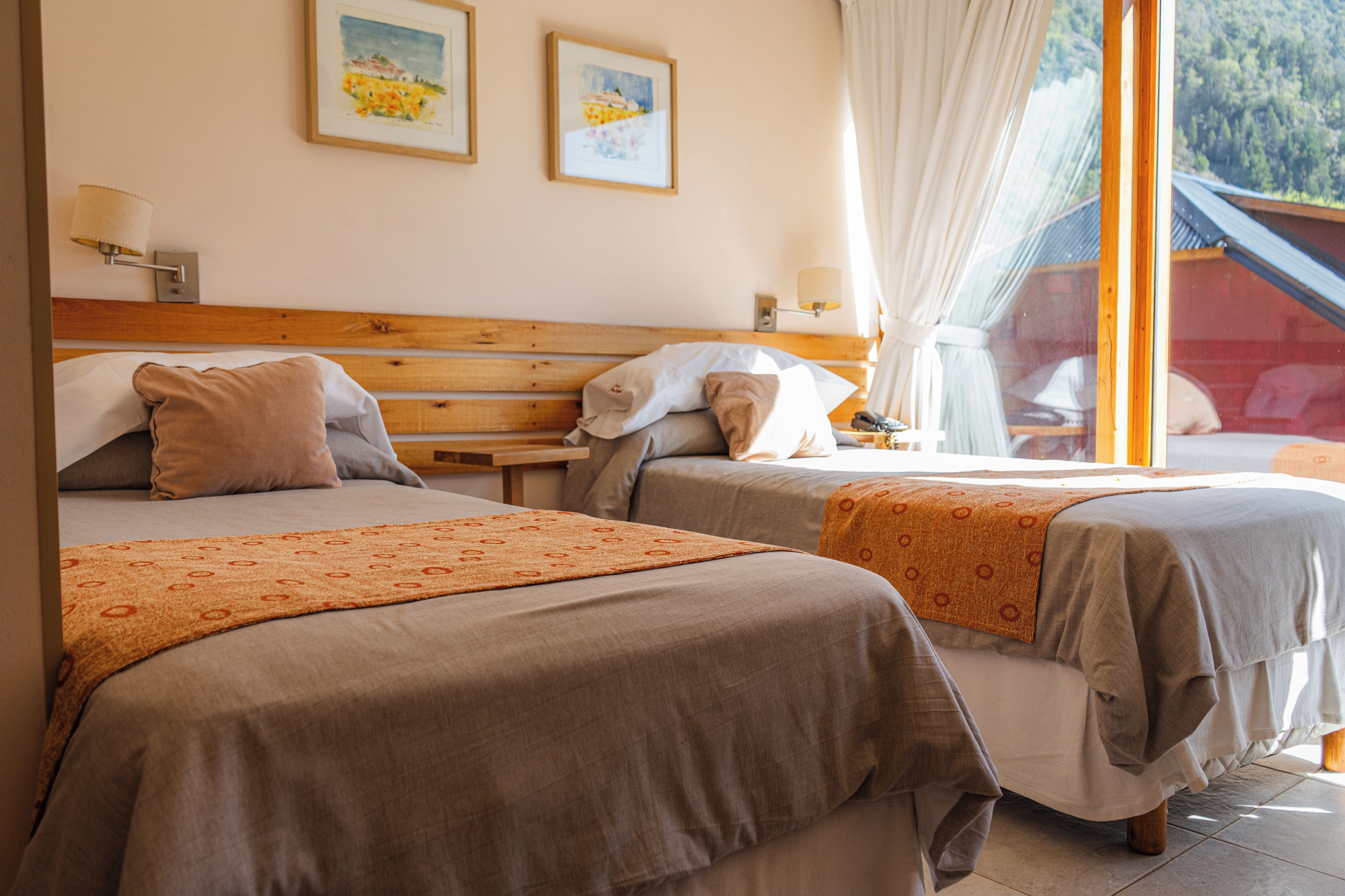 A hotel room with two beds, a wooden headboard, a nightstand, and a window with curtains.