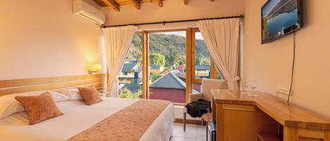Un dormitorio con cama, escritorio, silla, televisión y vistas a una montaña y edificios.