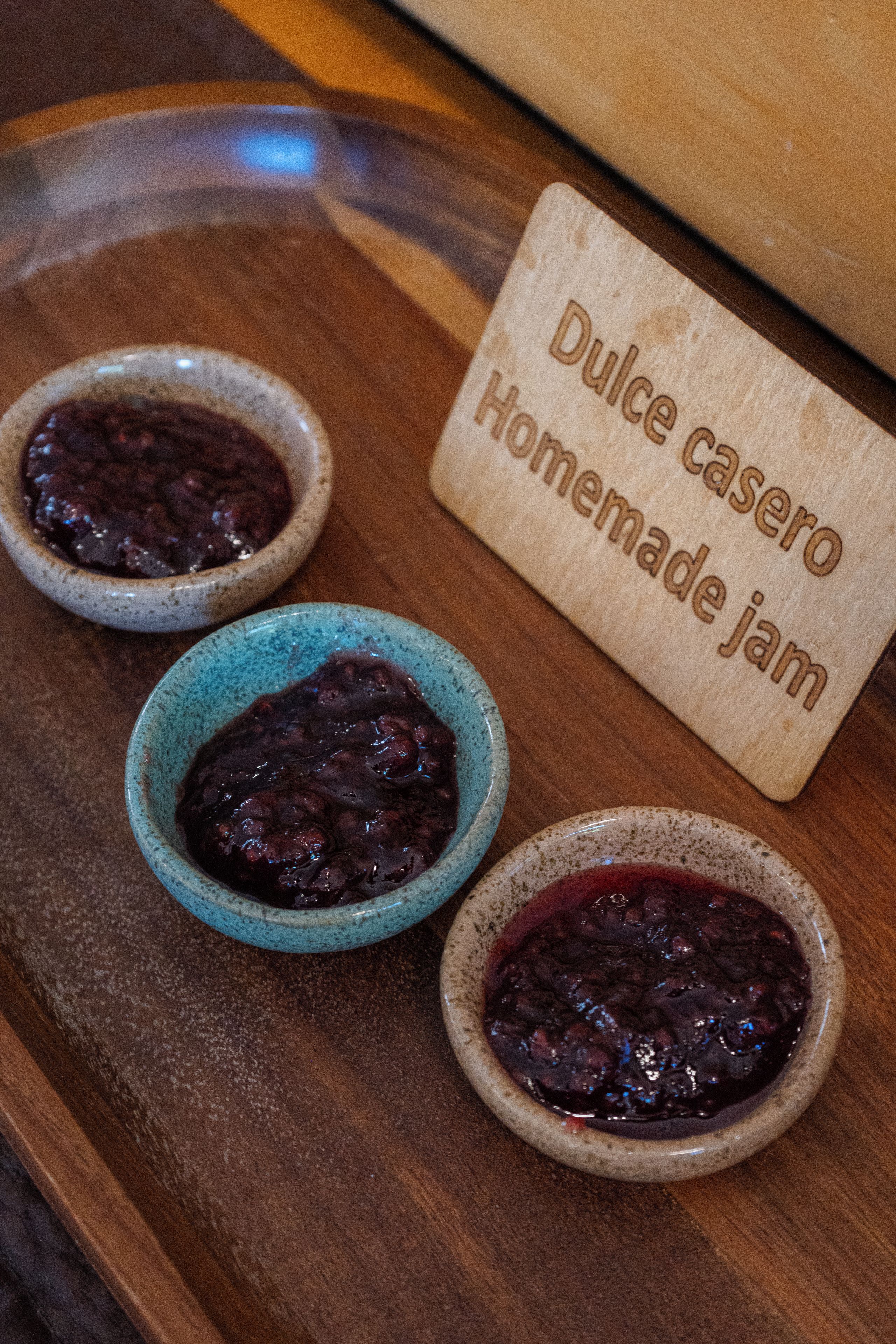 Three small bowls of homemade jam on a wooden tray with a label that reads 'Dulce casero Homemade jam.'