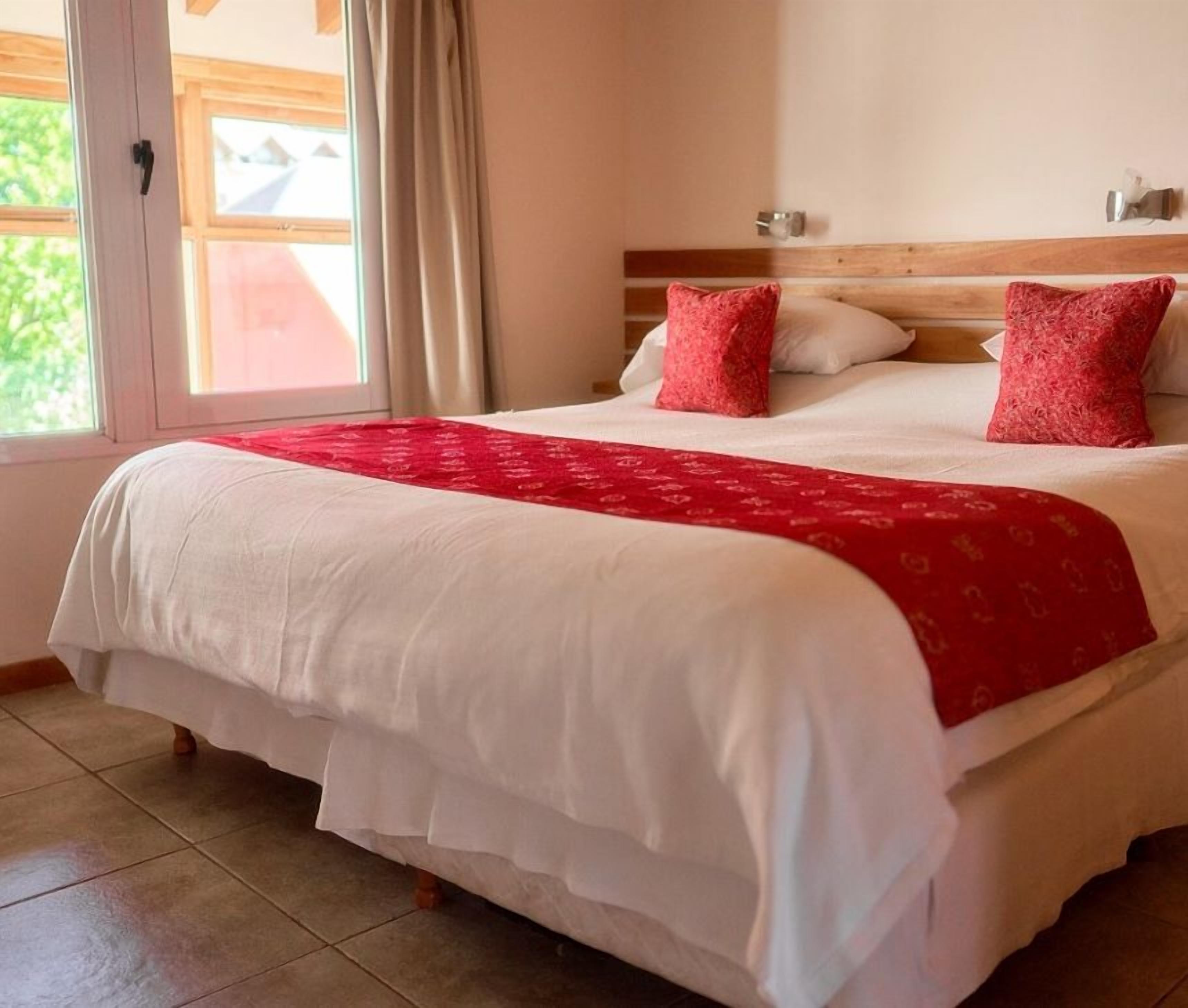 Une chambre d’hôtel avec un grand lit, une tête de lit en bois et une fenêtre avec des rideaux.
