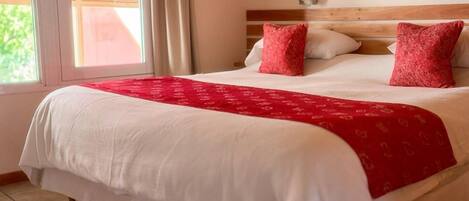 A hotel room with a large bed, a wooden headboard, and a window with curtains.