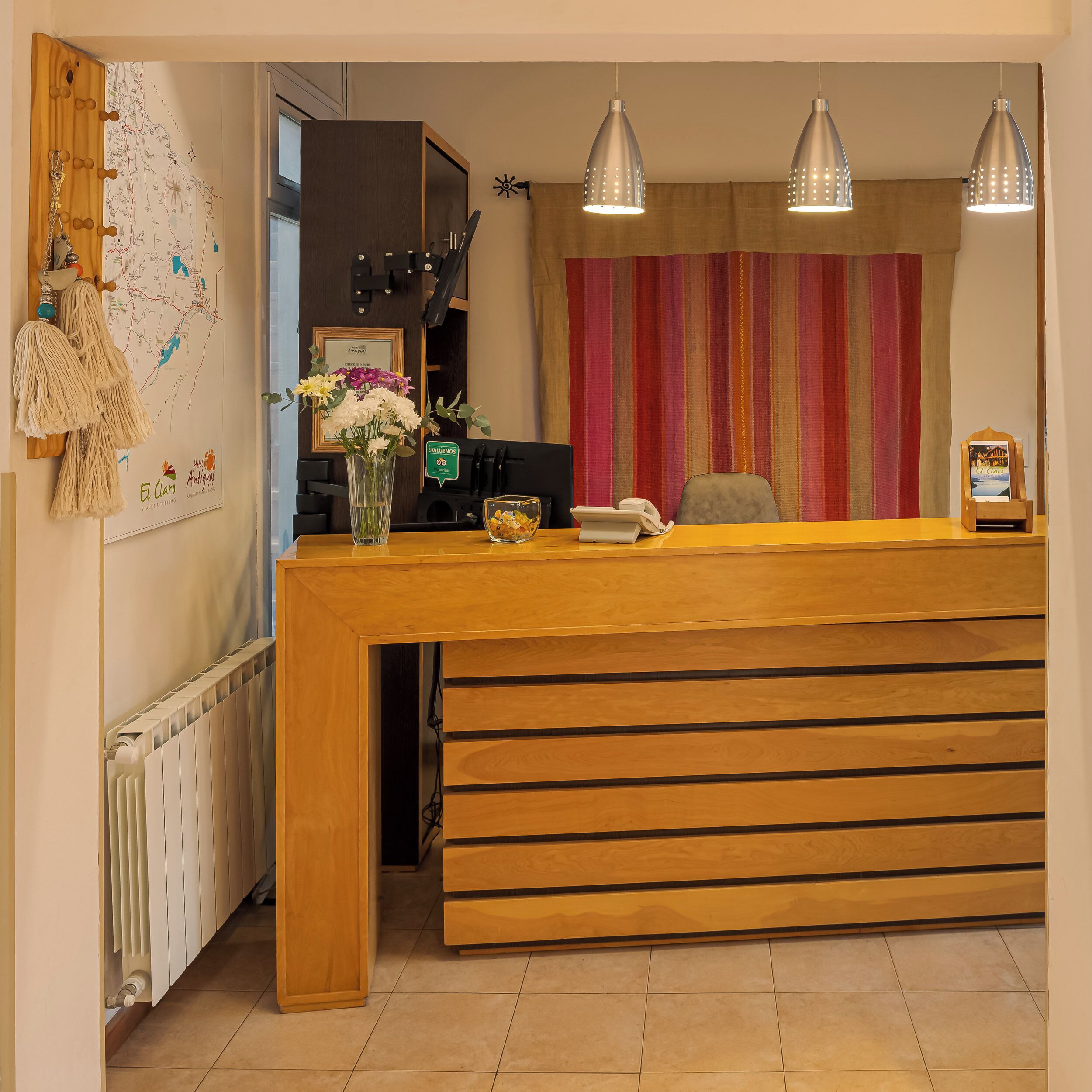 A reception desk with a wooden finish, a vase with flowers, a map on the wall, and a striped curtain.