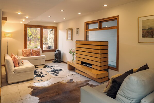 A modern living room with a sofa, a wooden entertainment unit, and a large window. - HOTEL ANTIGUOS (San Martín de los Andes)