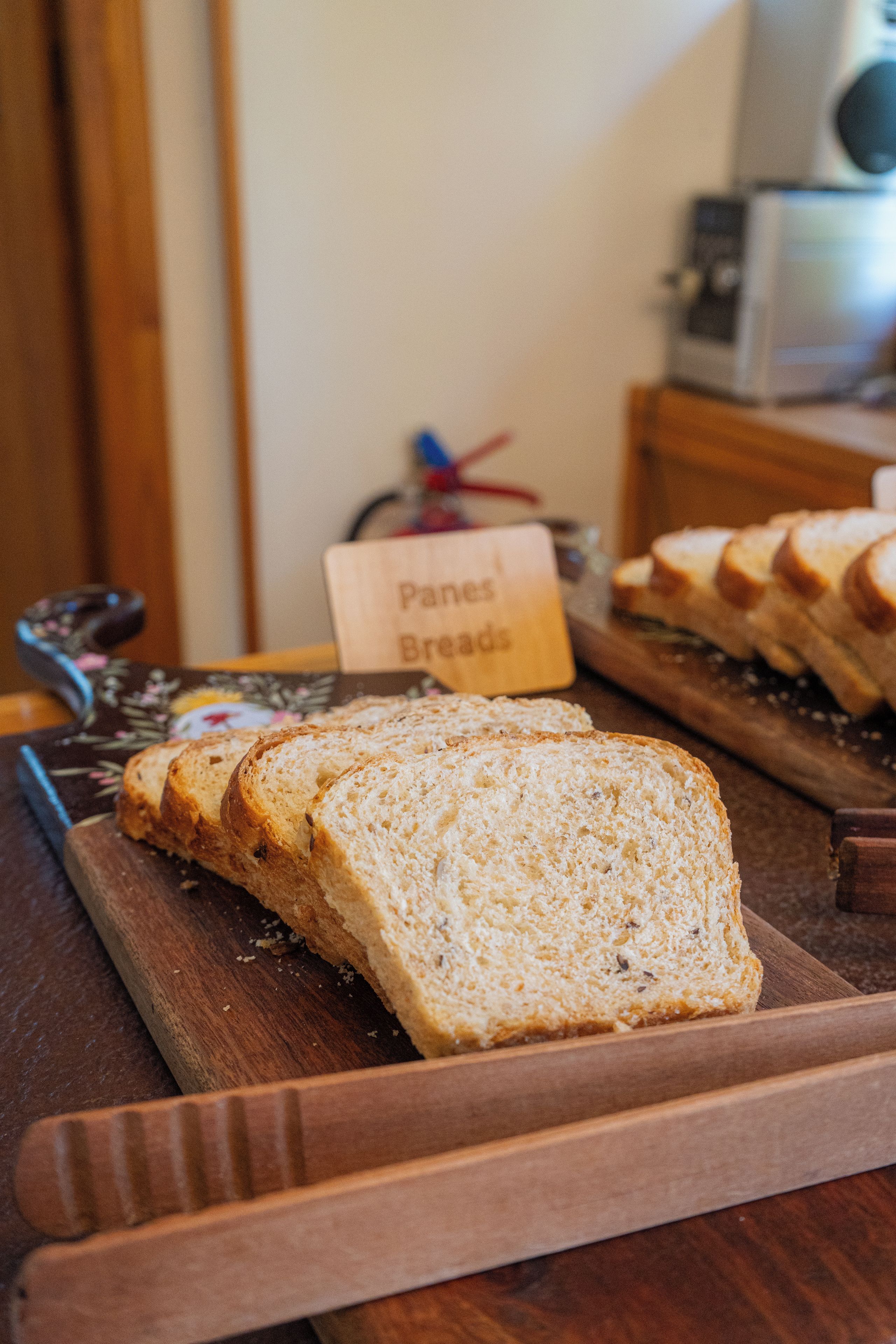 Slices of bread on a wooden board with a sign reading 'Panes Breads' in the background.