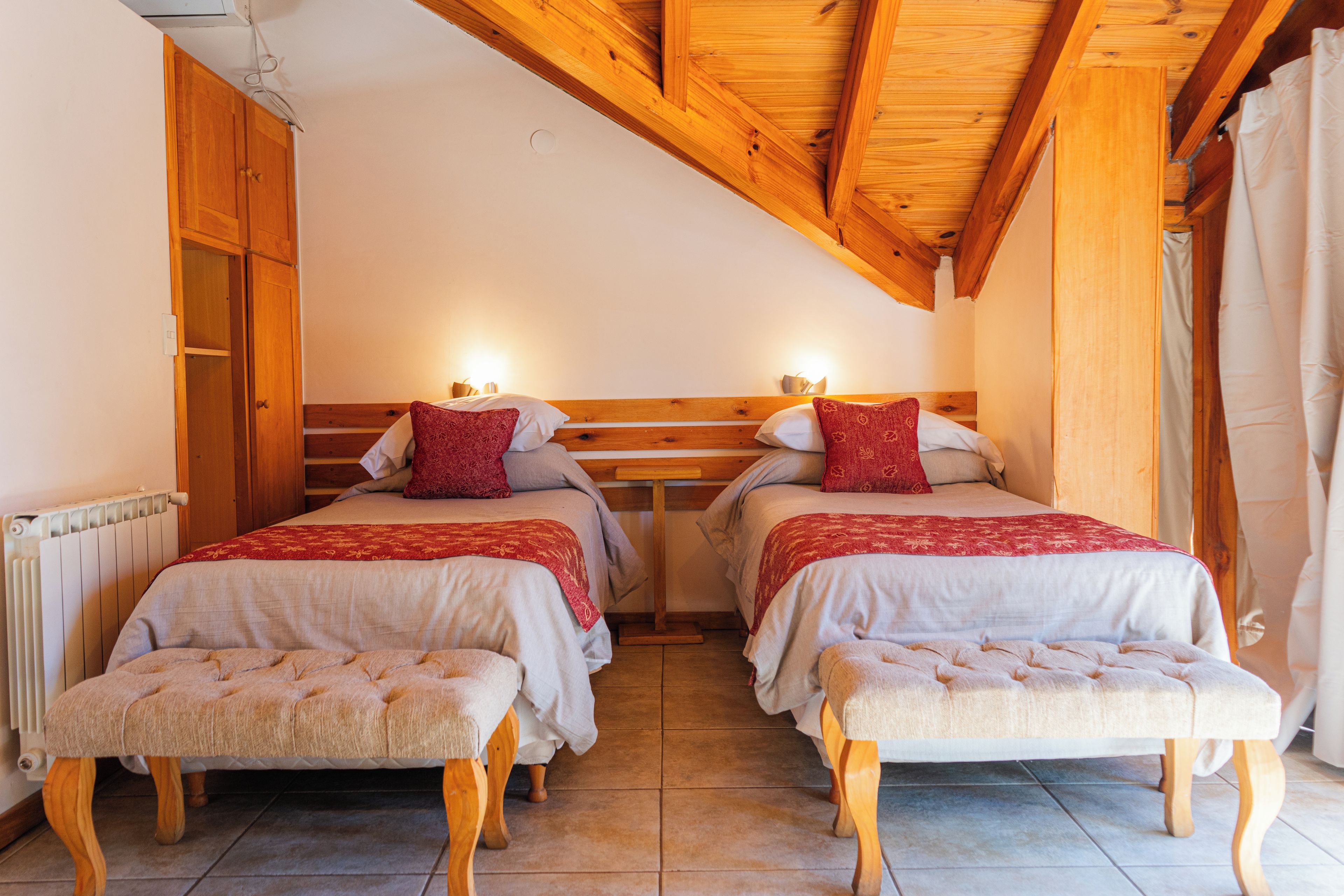 A room with two beds, wooden headboards, and a bench.