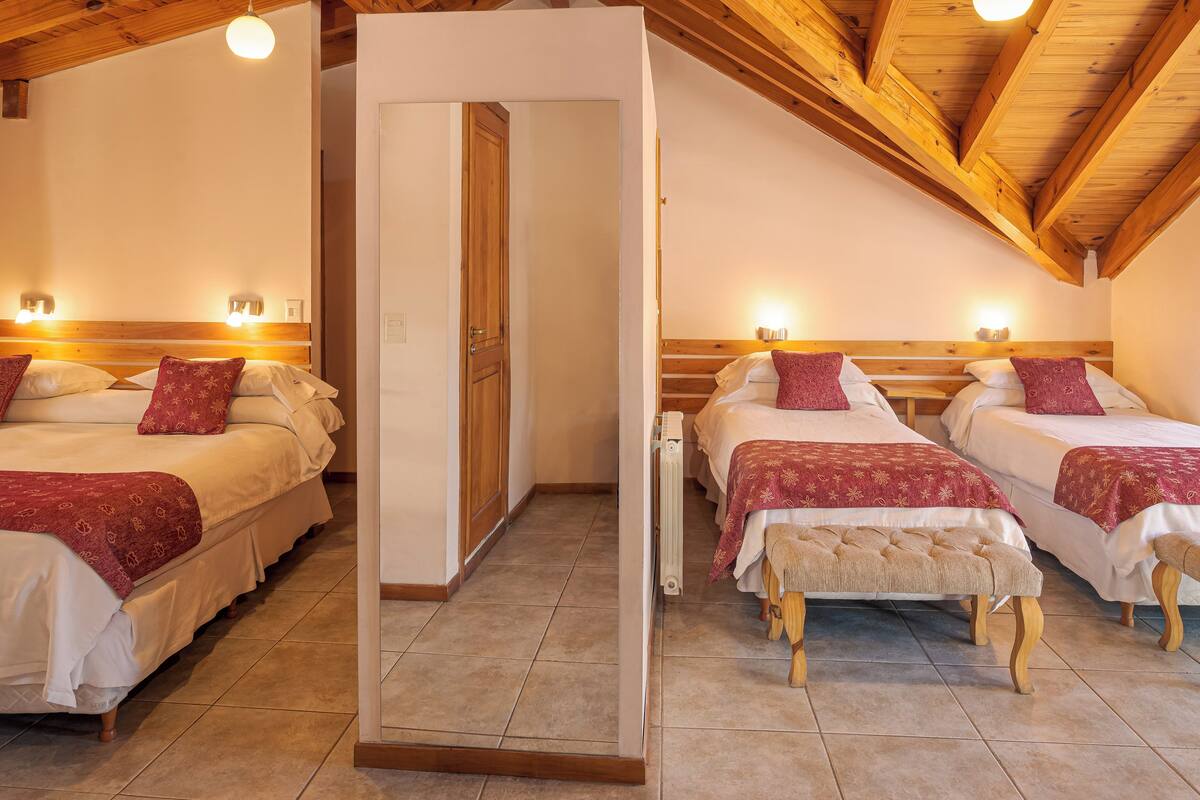 Une chambre d’hôtel avec deux lits, des poutres en bois au plafond et un banc placé entre les lits.