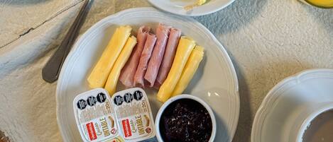 Une table de petit-déjeuner avec des assiettes contenant des œufs brouillés, du jambon, du fromage, un croissant et des toasts. On y trouve également deux verres de jus d’orange et une fleur dans un vase.
