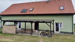 Een huis met een rood pannendak, een overdekt terras met bankjes en een fiets die ervoor staat.