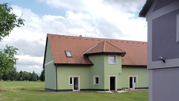 Een huis met twee verdiepingen, een rode dakbedekking en een groene buitenzijde.