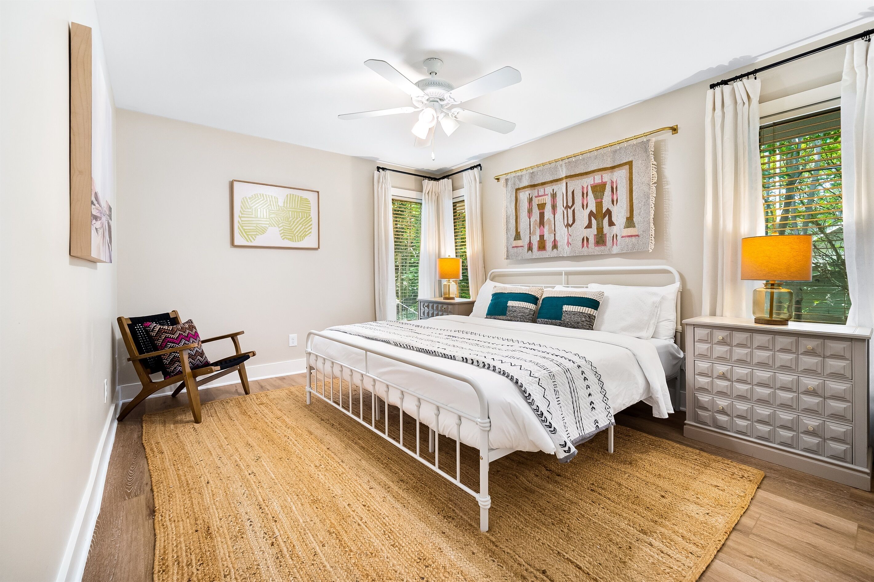 A bedroom with a bed, a ceiling fan, a window with curtains, a nightstand, and a chair.