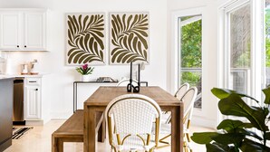 Una cocina moderna con armarios blancos, una mesa de comedor de madera y dos grandes obras de arte con motivos de hojas.