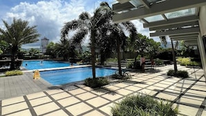 Zona de piscina con suelo de baldosas, palmeras y cielo despejado.