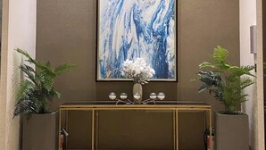 Un vestíbulo con piso de mármol, un cuadro abstracto de gran tamaño en la pared, una consola con un jarrón de flores y dos plantas en macetas.