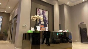 Una recepción moderna con un mostrador de vidrio, un cuadro abstracto de gran tamaño y un jarrón con flores.