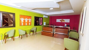 A reception area with a wooden desk, green chairs, and artwork on the walls. - Wakola business hotels (Dakar)