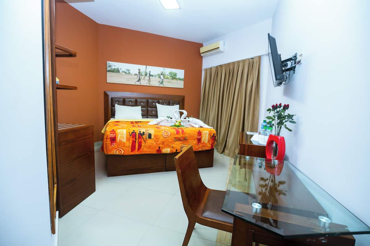 Une chambre d’hôtel avec un lit, un bureau, une chaise, une télévision et une fenêtre avec des rideaux.
