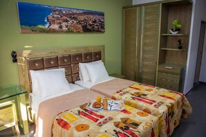 A hotel room with a bed, a glass table, a wooden wardrobe, and a painting of a coastal town. - Wakola business hotels (Dakar)