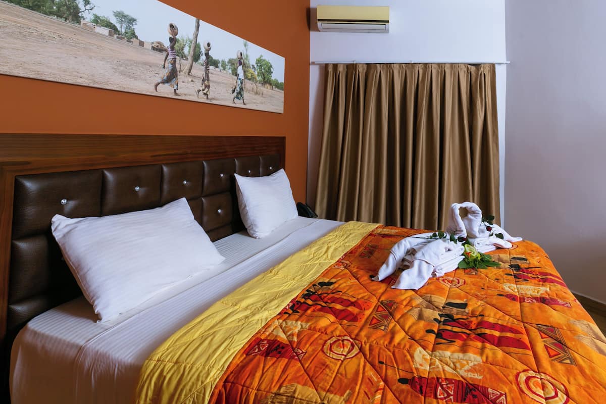 Une chambre d’hôtel avec un grand lit, une tête de lit, un tableau au mur et une fenêtre avec des rideaux.